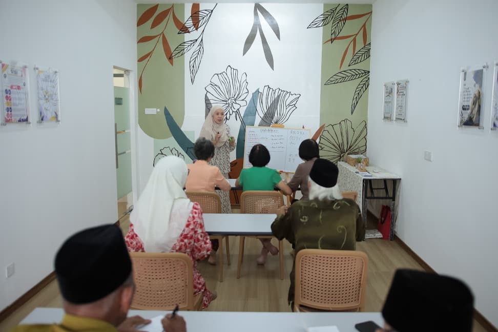 The class seated at their tables while the teacher works through the board at the front