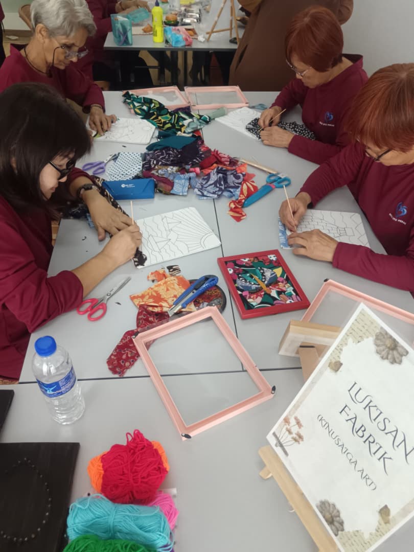 Participants pressing patterned fabric into carved panels, with a finished framed piece alongside