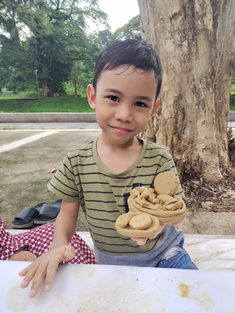 A boy holding up the clay piece he shaped, at an outdoor session
