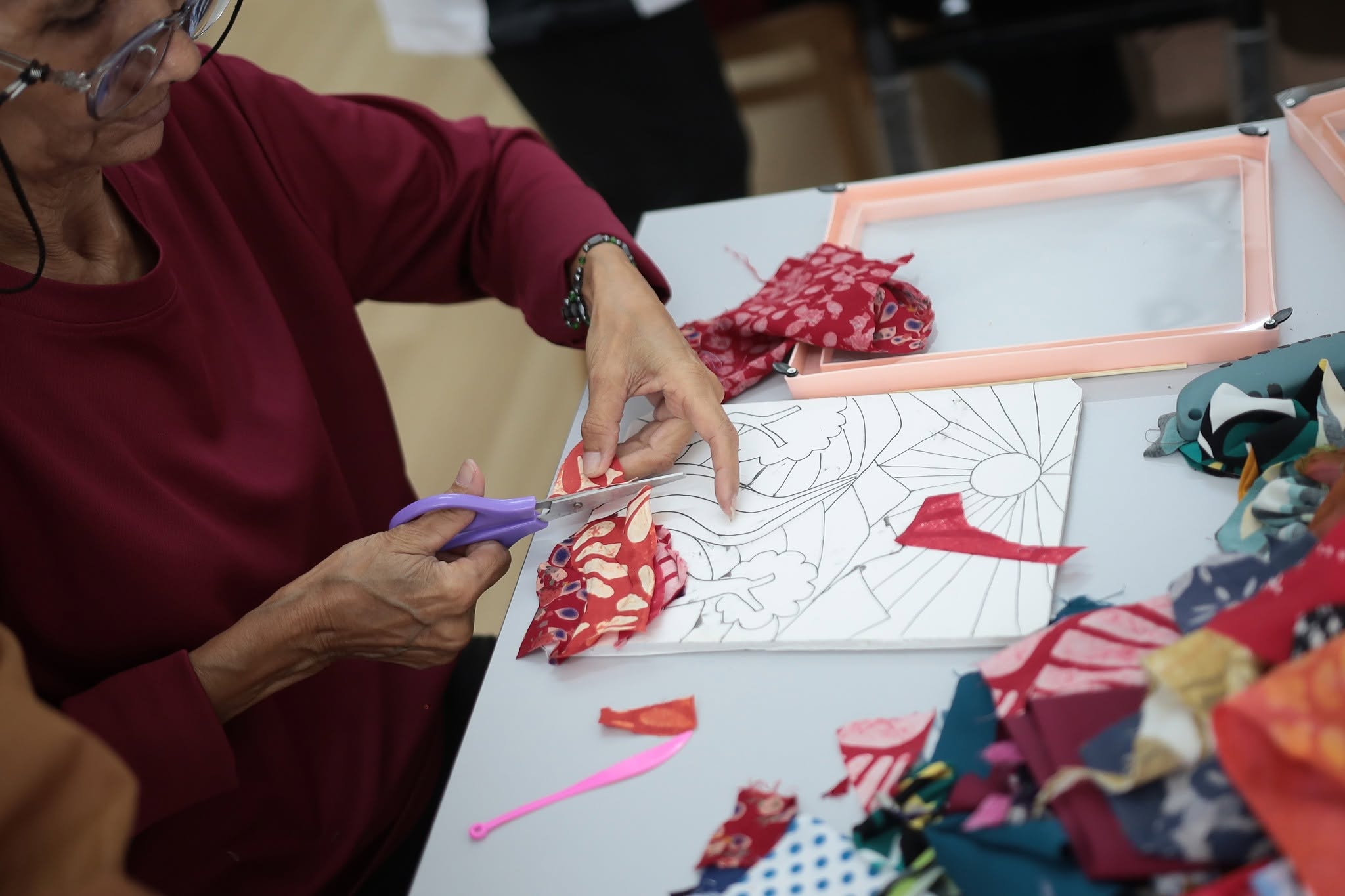 Close hands cutting patterned fabric during a guided craft session at Halaman Suri Sejahtera