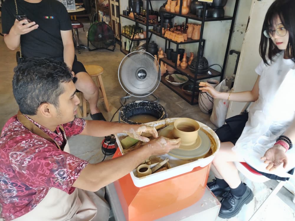A facilitator shaping clay on the wheel while a visitor watches, at Time Tunnel Ipoh Old Town